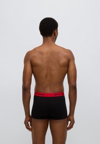 Μαύρα boxer briefs με κόκκινη ελαστική μέση που φέρει το λογότυπο "HUGO", ορατά από πίσω. Λείο υλικό και εφαρμοστό σχέδιο.