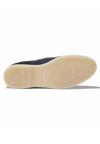 Suela de zapato de ante oscuro con una suela de goma que presenta patrones de agarre circulares y un logo en relieve. Goma color crema en los bordes.