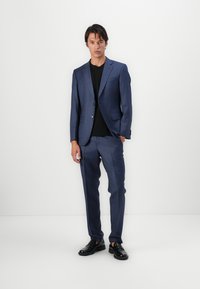 Traje azul marino con un sutil patrón de cuadros, americana de un solo botón y pantalones ajustados, combinados con una camisa negra y zapatos negros.