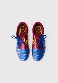 Chuteiras de futebol Nike com uma seção da ponta em couro azul, parte superior em bordeaux, logotipo preto, palmilha amarela com padrão circular e atacadores azuis.