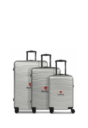 Three silver hardshell suitcases of varying sizes feature textured surfaces, black handles, and smooth-rolling wheels, with central logos.