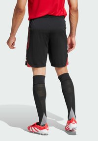 Schwarze Sportshorts mit roten Akzenten, kombiniert mit schwarzen knielangen Socken und roten Fußballschuhen mit weißen Streifen.
