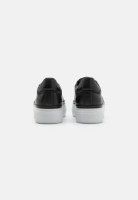 Baskets en cuir noir avec une semelle en caoutchouc blanc, présentant une texture lisse, un bout arrondi et un design minimaliste.