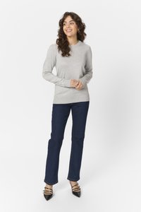 Maglione grigio chiaro a maniche lunghe con polsini e orlo a coste, abbinato a jeans dritti blu scuro e tacchi neri a punta con dettagli a strappo.