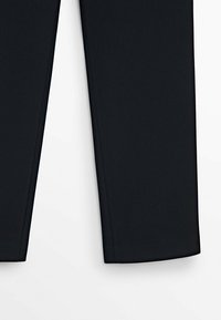 Mustat räätälöidyt housut esitettyinä keski-reidet alaspäin valkoisella taustalla.