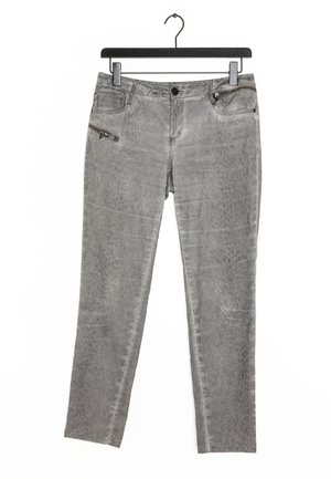 Pantalon en denim gris avec une texture imprimée serpent, comportant une poche zippée et des poches standard, suspendu à un cintre noir à pince.