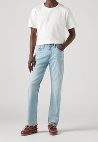 Vit bomullströja matchad med ljusblå denimjeans. Skorna är bordeauxfärgade med en texturerad läderfinish. Rakt snitt, utan mönster.