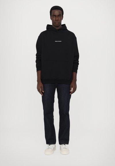 Sweat à capuche noir avec poche avant et texte blanc. Associé à un jean en denim foncé et des baskets blanches. Design simple et décontracté.
