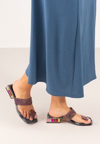 Sandalias de cuentas con una suela texturizada oscura, que cuentan con acentos de gemas coloridas en el tacón y una amplia tira colorida que cruza el pie.