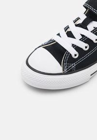 Fekete vászon sneaker fehér fűzőkkel, gumírozott orrral, fehér gumitalppal és fehér varrással. Klasszikus alacsony fazon.