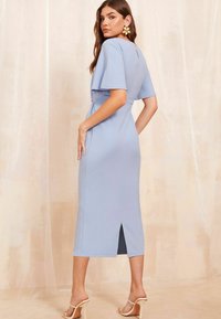 Abito midi azzurro chiaro con maniche corte, spacco laterale e vita aderente. Texture liscia e lieve lucentezza. Indossato con tacchi di colore chiaro.
