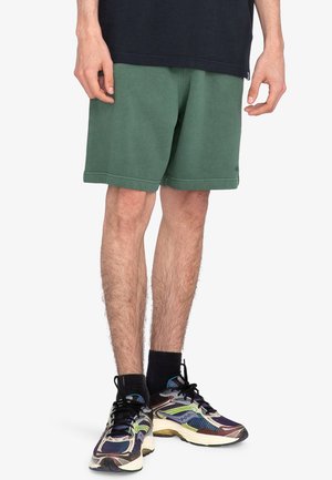 Grüne Baumwollmischung-Shorts mit relaxed Fit, ausgestattet mit einem elastischen Bund und seitlichen Taschen, kombiniert mit mehrfarbigen Sportschuhen.