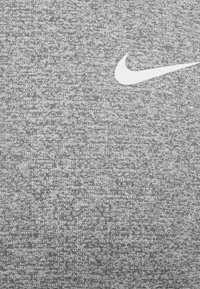 Grå atletisk tyg med ett strukturerat mönster; har en vit Nike-logotyp som accent på övre vänstra delen.