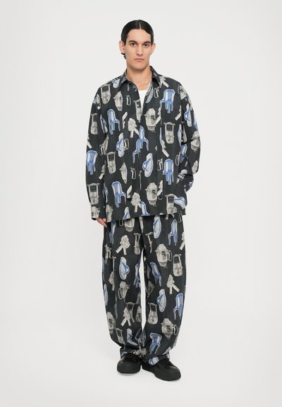 Tenue noire à motifs comprenant une chemise et un pantalon. Le design inclut des représentations abstraites grises et bleues de chaises et d'outils. Coupe ample, tissu léger.