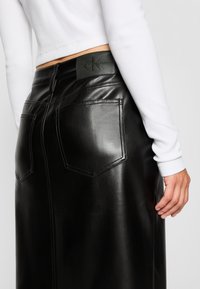 Zwarte faux leren rok met twee achterzakken, zichtbare stiksels en een merklabel in de taille. Gladde, glanzende afwerking.