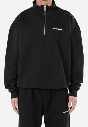 Pull en polaire noir avec un col montant et une fermeture éclair quart. Comprend des poignets côtelés et un logo sur le devant, associé à un pantalon de survêtement noir assorti.