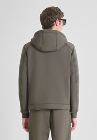 Hoodie aus gedämpftem grünem Stoff mit sichtbaren Nähdetails, gerippten Bündchen und lockerer Passform. Die Rückansicht zeigt die Kapuze und klare Linien.