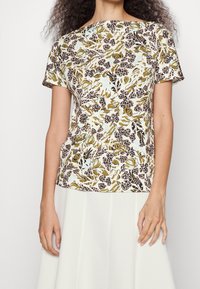 Top de manga corta con estampado floral que presenta un fondo azul claro con patrones botánicos en verde y marrón, fabricado en tejido suave y transpirable.