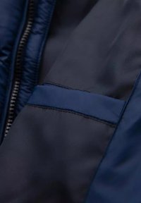 Tessuto di giacca blu navy con una texture liscia e lucida. Presenta una chiusura frontale con zip e una piccola tasca inclinata con cuciture a contrasto.