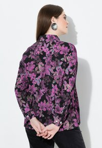 Camicia floreale nera, con fiori viola e turchesi, maniche lunghe, polsini con bottone e colletto. Tessuto strutturato.