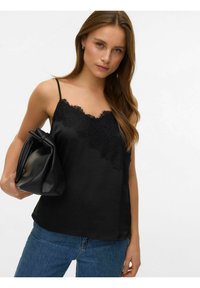 Sort satengcamisole med blonder ved utringningen, tynne justerbare stropper, kombinert med en svart skinnveske og blå denimjeans.