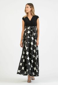 Maxi-jurk met een zwart aansluitend lijfje en een vloeiende rok met grote zwart-witte stippen. Knoopdetail in de taille.