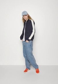 Meresinine pommitaja jope valgete triipudega, kombineeritud helesiniste teksade ja oranžide tossudega. Sinine nokamüts, lõdvestunud istuvus ja minimalistlik disain.