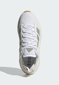 Zapatilla deportiva blanca con parte superior de malla, rayas grises y suela de goma. Cuenta con cierre de cordones y cuello acolchado. Detalle texturizado en la lengüeta.