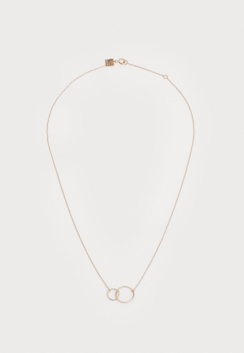 Collar en tono dorado con una cadena ajustable, dos círculos entrelazados y un cierre con una pequeña etiqueta. Textura suave y diseño minimalista.