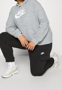 Grå huvtröja med en stor vit Nike-logga, svarta joggerbyxor med uppvikta ben och en cargo ficka, samt flerfärgade Nike-sneakers med en strukturerad design.