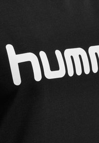 T-shirt nera con grande testo bianco che legge "humm", caratterizzata da una texture liscia e un font arrotondato e moderno.