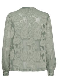 Sheer green blouse with floral embroidery, long sleeves, and buttoned cuffs. Soft texture, lightweight fabric with a delicate pattern.