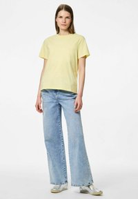 T-shirt giallo chiaro a maniche corte abbinato a jeans azzurri larghi e scarpe in metallo argentato. Design semplice con una vestibilità comoda.