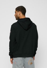 Sort hoodie med en stor hætte, ribbede manchetter og justerbare snore. Har logo på højre ærme og blød, tekstureret stof.