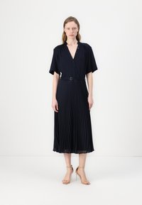 Navy pleated dress with a V-neck, short sleeves, and a belted waist. Smooth texture with a flowing silhouette extending to the mid-calf.