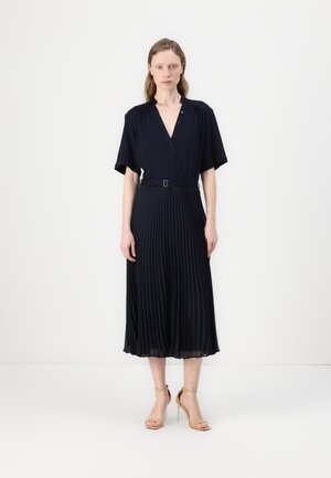 Navy pleated dress with a V-neck, short sleeves, and a belted waist. Smooth texture with a flowing silhouette extending to the mid-calf.