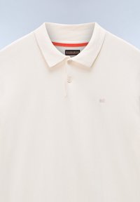 Crème polo shirt met een zachte textuur, klassieke kraag, twee knopen en een klein geborduurd logo op de borst, met een rode accent binnenin de kraag.