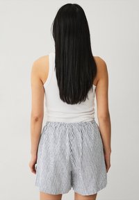 Débardeur blanc à coupe décontractée, associé à un short rayé bleu et blanc, doté d'une ceinture élastique et d'une silhouette ample.