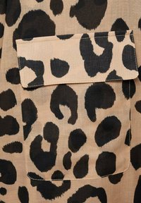 Bežna tekstilna površina s velikimi črnimi lisami leoparda in podrobnostjo žepa na prsih. Tkanina se zdi lahka z gladko teksturo.