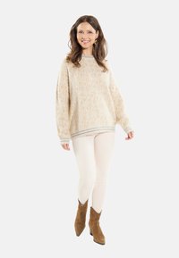 Maglione beige a maglia con texture decorativa, vestibilità ampia e polsini a costine. Abbinato a pantaloni chiari e stivaletti alla caviglia in camoscio marrone.