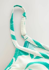 Vícebarevný ramínek tílka s tyrkysovým a bílým listovým vzorem, vyrobený z měkké látky s prošívanými detaily a nastavitelným kováním.