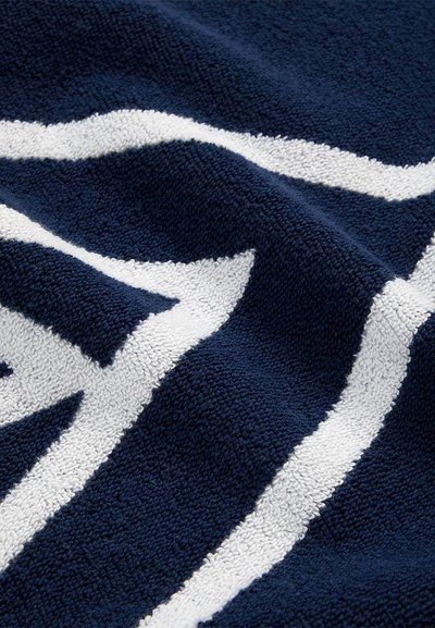 Κοντινό πλάνο υφάσματος σε ναυτικό μπλε με υφή και ανεβασμένα λευκά γεωμετρικά σχέδια σε ρίγες που σχηματίζουν γωνιώδη σχήματα.