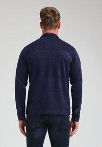 Giacca in suede blu navy con maniche lunghe, polsini con bottoni e una texture liscia. Presenta un colletto strutturato e un design posteriore pulito.