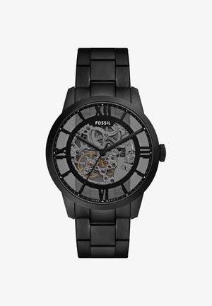 Black Fossil automatic wristwatch with skeleton dial showing inner gears, black metal link band, and Roman numeral hour markers.