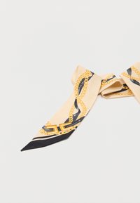 Μπεζ μεταξωτό φουλάρι με σχέδιο από χρυσή αλυσίδα και αγκράφα, μερικώς τυλιγμένο, που βρίσκεται πάνω σε λευκή επιφάνεια.