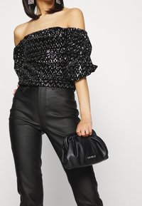 Mustat paljeteilla koristellut olkapäiltä avoimet yläosat puffihihnoilla yhdistettynä korkeavyötäröisiin mustiin tekonahkahousuihin. Malli pitää mustaa nahkalaukkua.