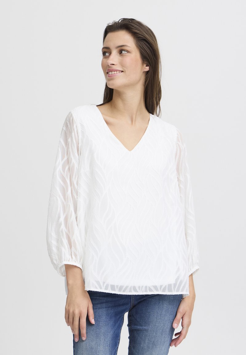 Weißes V-Ausschnitt-Bluse mit strukturiertem Blattmuster, langen transparenten Ärmeln und elastischen Bündchen; kombiniert mit blauen Jeans.
