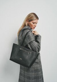 Czarna skórzana torba tote z teksturowanym wykończeniem, z przednią kieszenią na zamek błyskawiczny i długim paskiem. Projekt jest prosty i funkcjonalny.