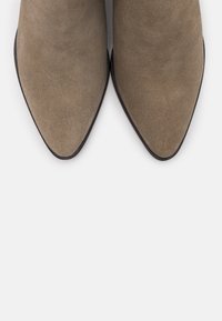 Stivali alla caviglia in suede beige con punta affusolata e texture liscia, caratterizzati da un tacco nero basso e senza decorazioni visibili.