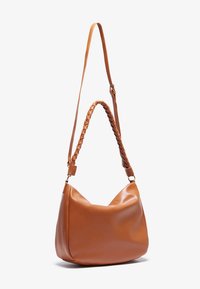 Sac à épaule en cuir tan avec une texture douce et lisse. Il est doté d'une bandoulière tressée et d'une forme arrondie et décontractée. Longueur de l'épaule ajustable.